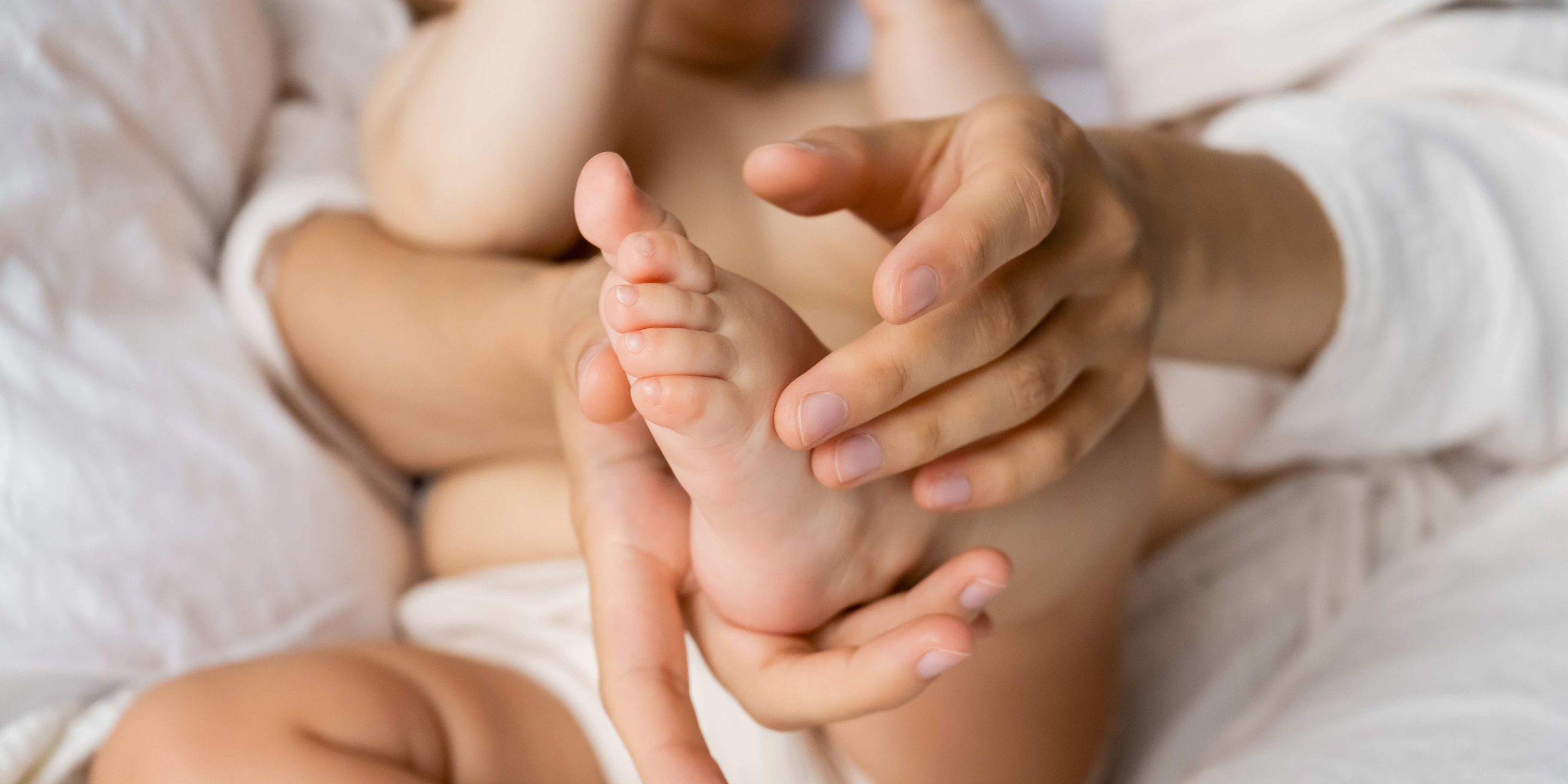 Cropped view of mother touching foot of baby daughter on bed.