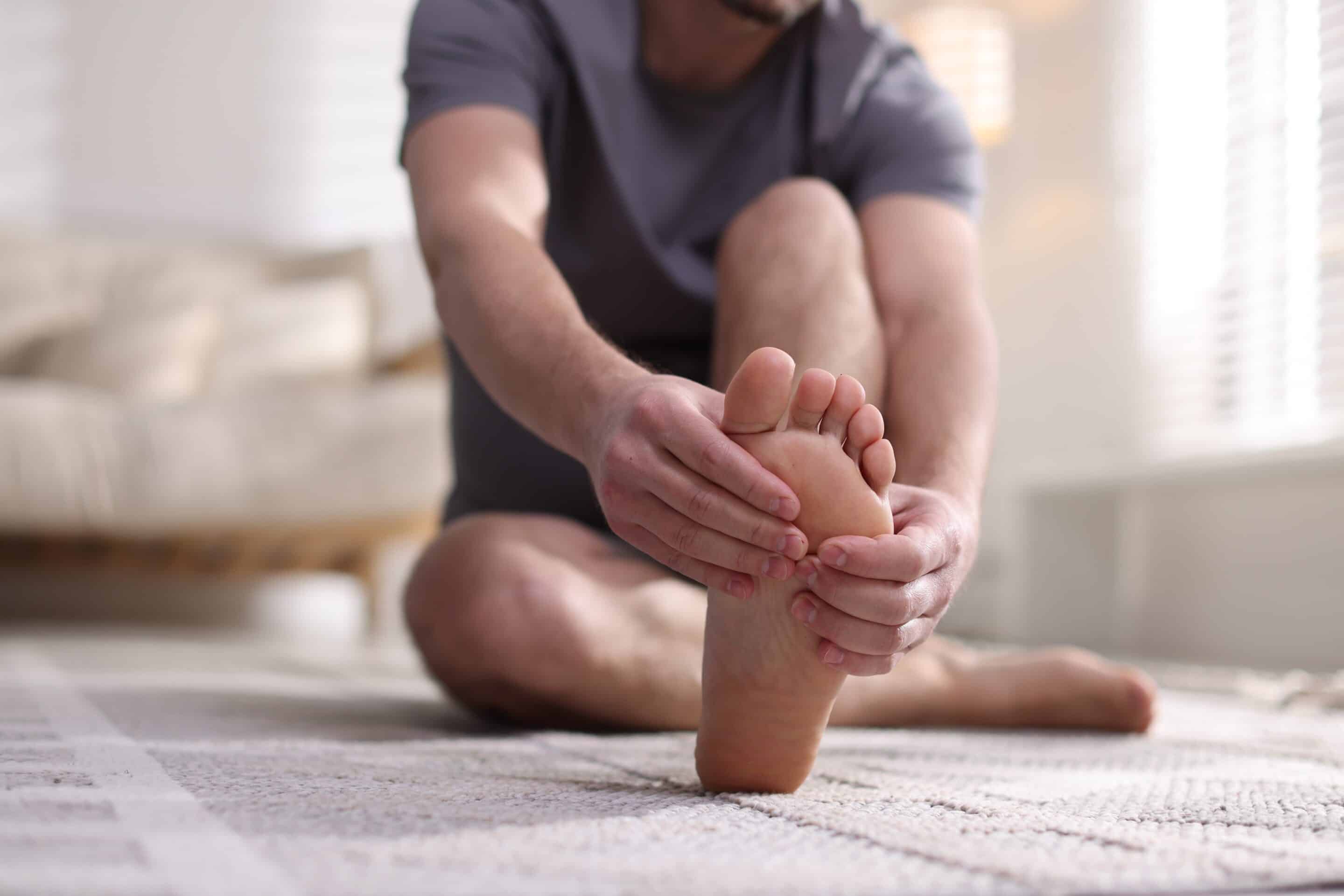 Man suffering from pain in foot on floor at home, closeup